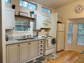 Una cocina con armarios blancos, un microondas, estufa y un reloj en la pared.