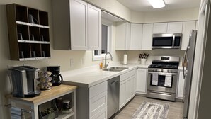 Una cocina moderna con armarios blancos, estufa de acero inoxidable, microondas y cafetera.