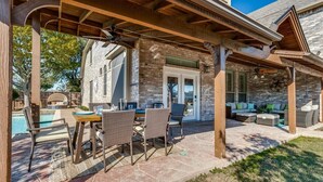 A covered patio area with stone flooring, wicker furniture, and a stone building in the background.