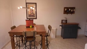 A dining area with a wooden table, four chairs, a hanging light fixture, a framed artwork, a small decorative item, and a kitchen area with cabinets and a countertop. - Two Bedroom Private Apt near NYC! (West New York)