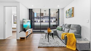 Una sala de estar moderna con un sofá gris, un televisor y vistas a un edificio a través de puertas de cristal.