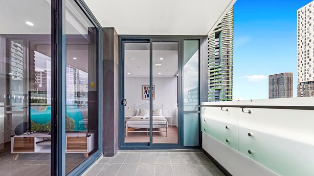 Un hotel moderno con balcón, una cama, un televisor y vistas de la ciudad.