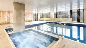 Una piscina interior moderna con paredes de vidrio transparente, suelo de baldosas y escalera de metal.