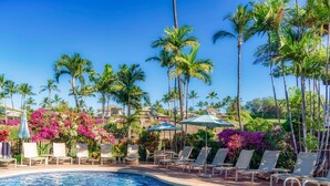 A swimming pool with lounge chairs and umbrellas, surrounded by palm trees and colorful flowers. - Aloha Moon - The Honeymoon Hideaway (Wailea)