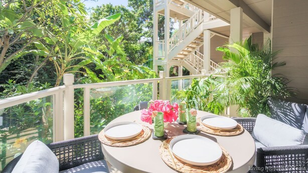 A round table with plates, cutlery, and a vase of flowers on a balcony with a view of a staircase and greenery. - Aloha Moon - The Honeymoon Hideaway (Wailea)
