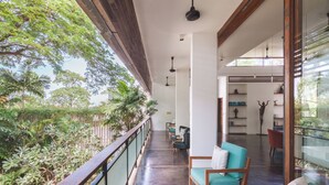 A balcony with a view of lush greenery, a seating area with chairs and a sofa, and a modern interior with shelves and a statue. - 5BR Designer Eco-Villa, Private Pool (Krong Siem Reap)
