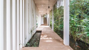 A corridor with a concrete floor, white columns, and a water feature running parallel to the walls. - 5BR Designer Eco-Villa, Private Pool (Krong Siem Reap)