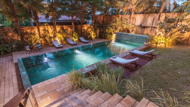 A rectangular swimming pool with a wooden deck and lounge chairs, surrounded by a wooden fence and lush greenery. - 5BR Designer Eco-Villa, Private Pool (Krong Siem Reap)