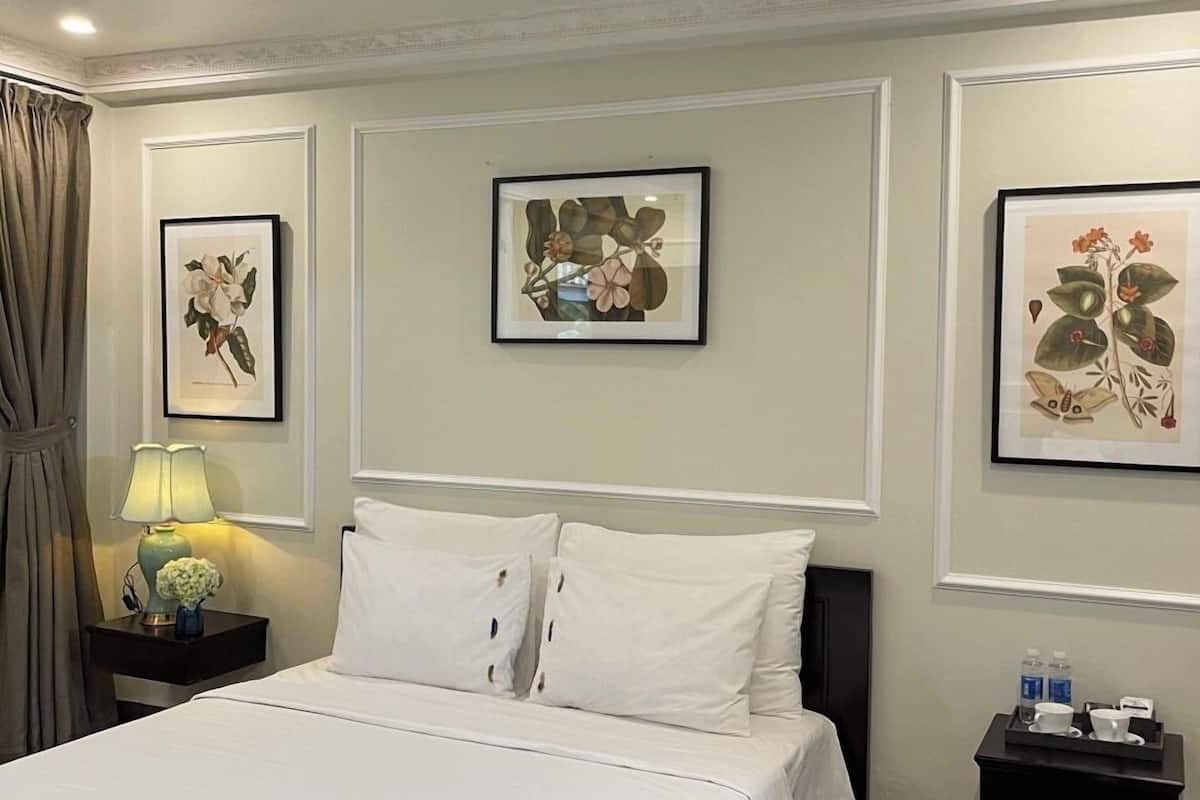 A hotel room with a large bed, two bedside tables, a nightstand, and three framed botanical prints on the wall.
