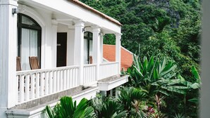 Un bâtiment de style colonial, peint en blanc, doté d’un balcon et entouré d’une végétation tropicale luxuriante.