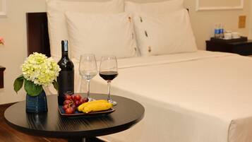 Un letto rifatto con lenzuola bianche, un tavolino con una bottiglia di vino, due bicchieri e un piatto di frutta.