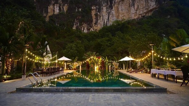 Un espace piscine agrémenté de tables et de chaises, illuminé de guirlandes lumineuses et offrant une vue sur un paysage montagneux.