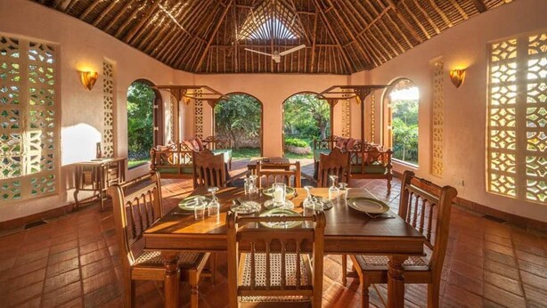A dining area with a thatched roof, wooden furniture, and natural light from arched windows.