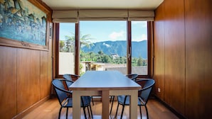 A conference room with a wooden table and chairs, large windows with a view of mountains and greenery. - Bedugul Lake View Villa (Buleleng)