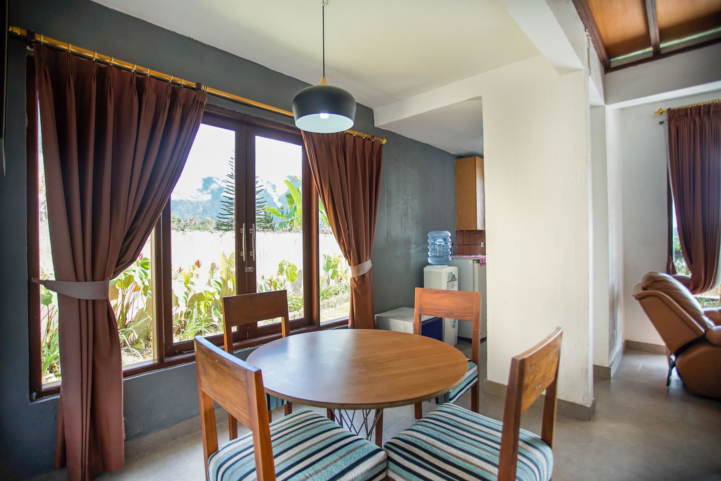 A dining area with a round wooden table, striped cushioned chairs, and brown curtains.