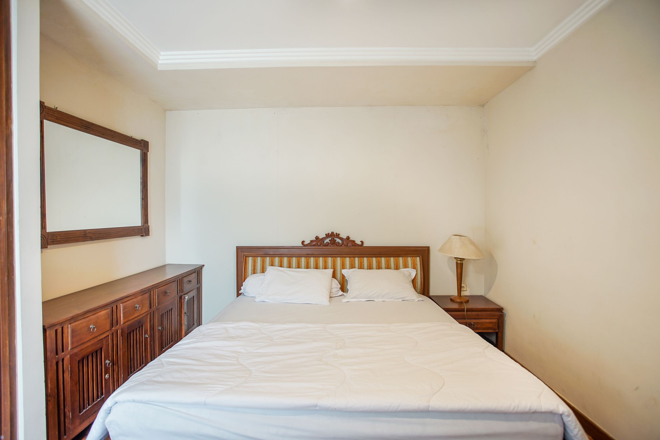 Un dormitorio con una cama de madera, una mesita de noche con lámpara y un aparador.
