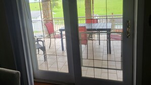 A view through a screened door of a patio area with a table and chairs, a stone pillar, and a grassy field in the background. - Quiet Space with Spacious Yard for Parking in Nice Community  (East Millsboro)
