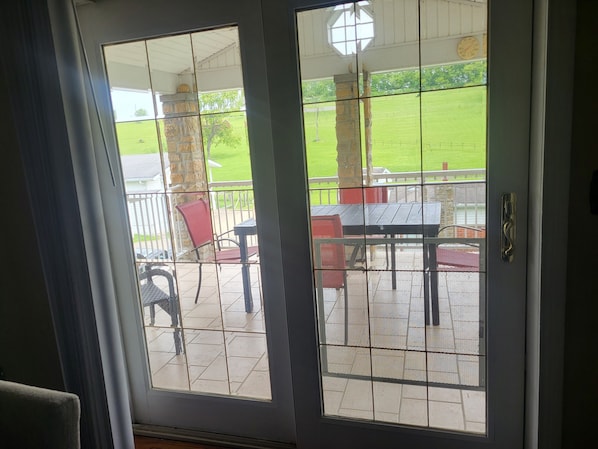 A view through a screened door of a patio area with a table and chairs, a stone pillar, and a grassy field in the background. - Quiet Space with Spacious Yard for Parking in Nice Community (East Millsboro)