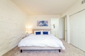 A bedroom with a bed, a nightstand, a wall-mounted lamp, and a door leading to another room.
