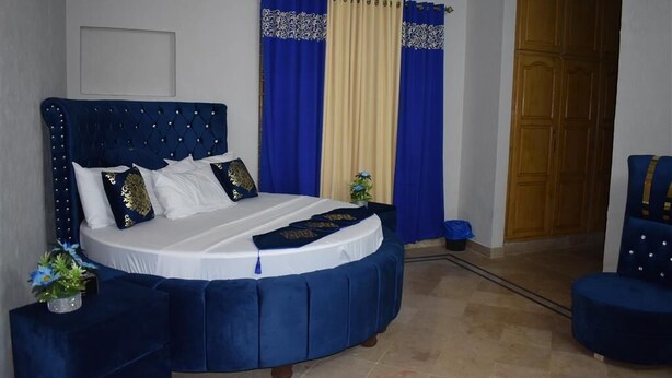 A bedroom with a large bed, a blue upholstered chair, and a wooden wardrobe. - Galaxy Lodge  (Islamabad)