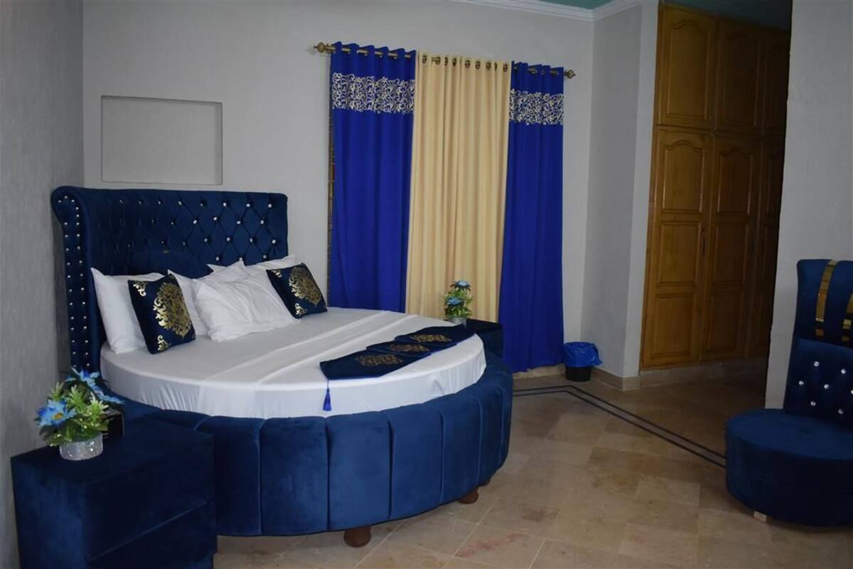 Une chambre à coucher avec un grand lit, un fauteuil bleu recouvert de tissu et une armoire en bois.