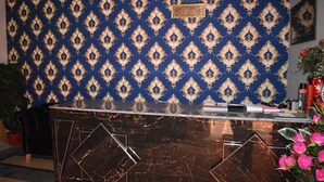 A reception desk with a dark marble top and a patterned blue and gold wallpaper background. - Galaxy Lodge  (Islamabad)