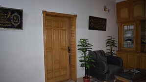 A room with a wooden door, a black sofa, a red potted plant, and a glass coffee table. - Galaxy Lodge  (Islamabad)
