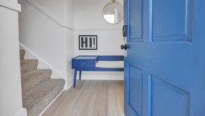 Eine Treppe mit Teppichstufen führt zu einem Raum, der eine blaue Tür, eine weiße Wand und einen kleinen, blauen Schreibtisch mit weißem Kissen hat.