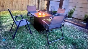 Eine Außenpatio mit einem Metalltisch und -stühlen, einem Feuerkorb und einem Holzzaun im Hintergrund.