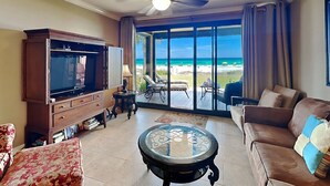 A living room with a television, a coffee table, a sofa, and a view of the beach. - Ground-Floor Condo – Romar House 103B, Gulf-Front! (Orange Beach)