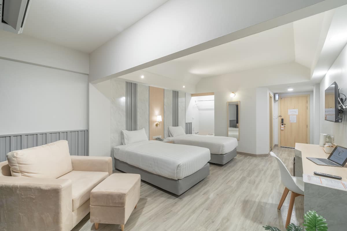 Une chambre d’hôtel moderne équipée d’un canapé, de deux lits, d’un bureau et d’une télévision.
