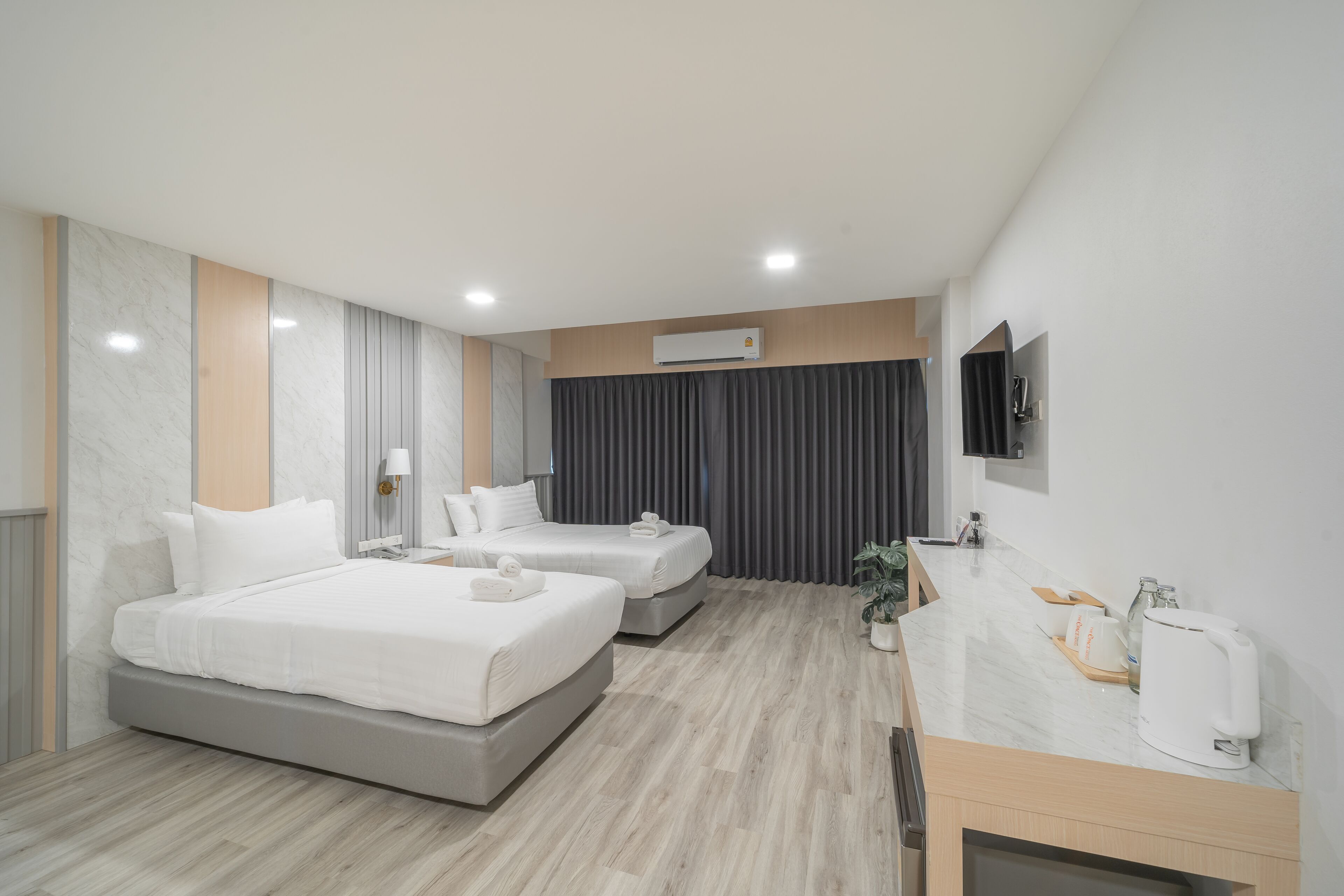 Quarto de hotel moderno com duas camas, televisão de tela plana, escrivaninha com cafeteira e ar condicionado.