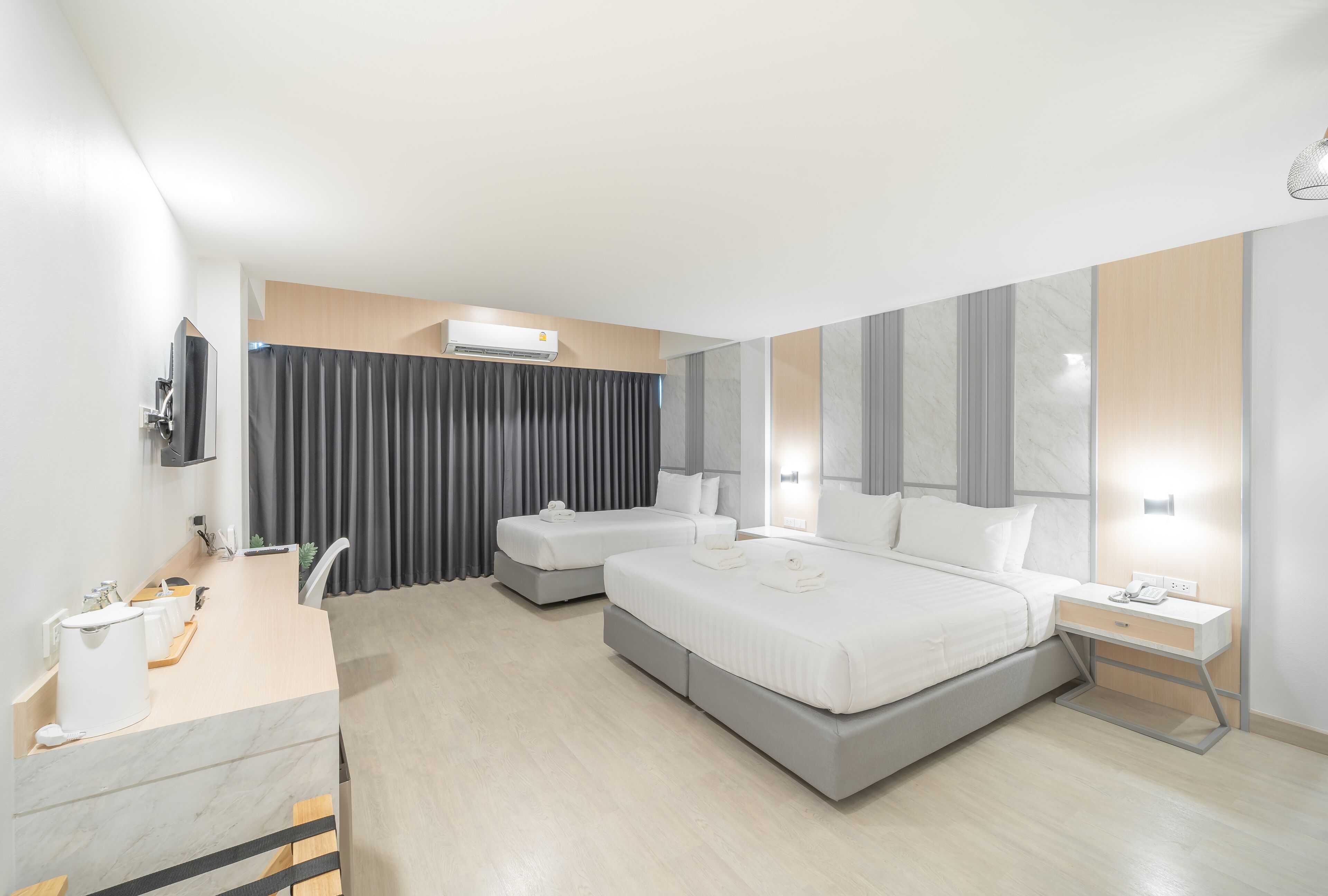 A modern hotel room with a large bed, a bedside table, a desk with a chair, a TV, and a bathroom with a mirror and sink.