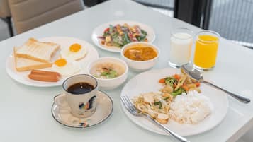 A table with plates of food, including rice, vegetables, and eggs, along with a cup of coffee and two glasses of orange juice.