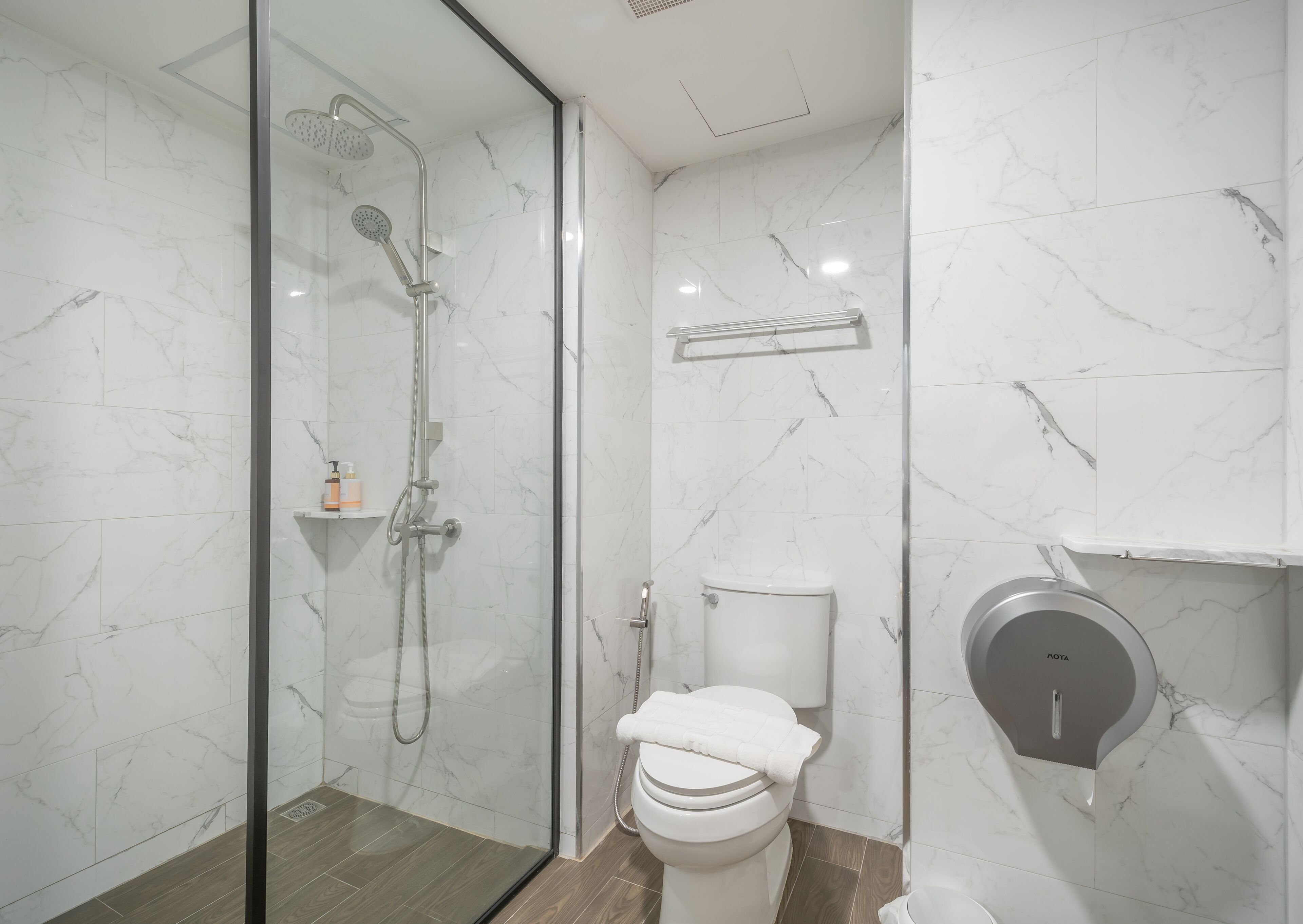 A modern bathroom with a glass-enclosed shower, a toilet, and a hand dryer.