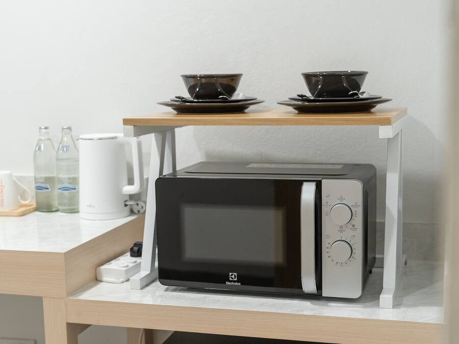 A compact microwave oven with a digital display, a control panel with multiple settings, and a small water bottle on the counter.