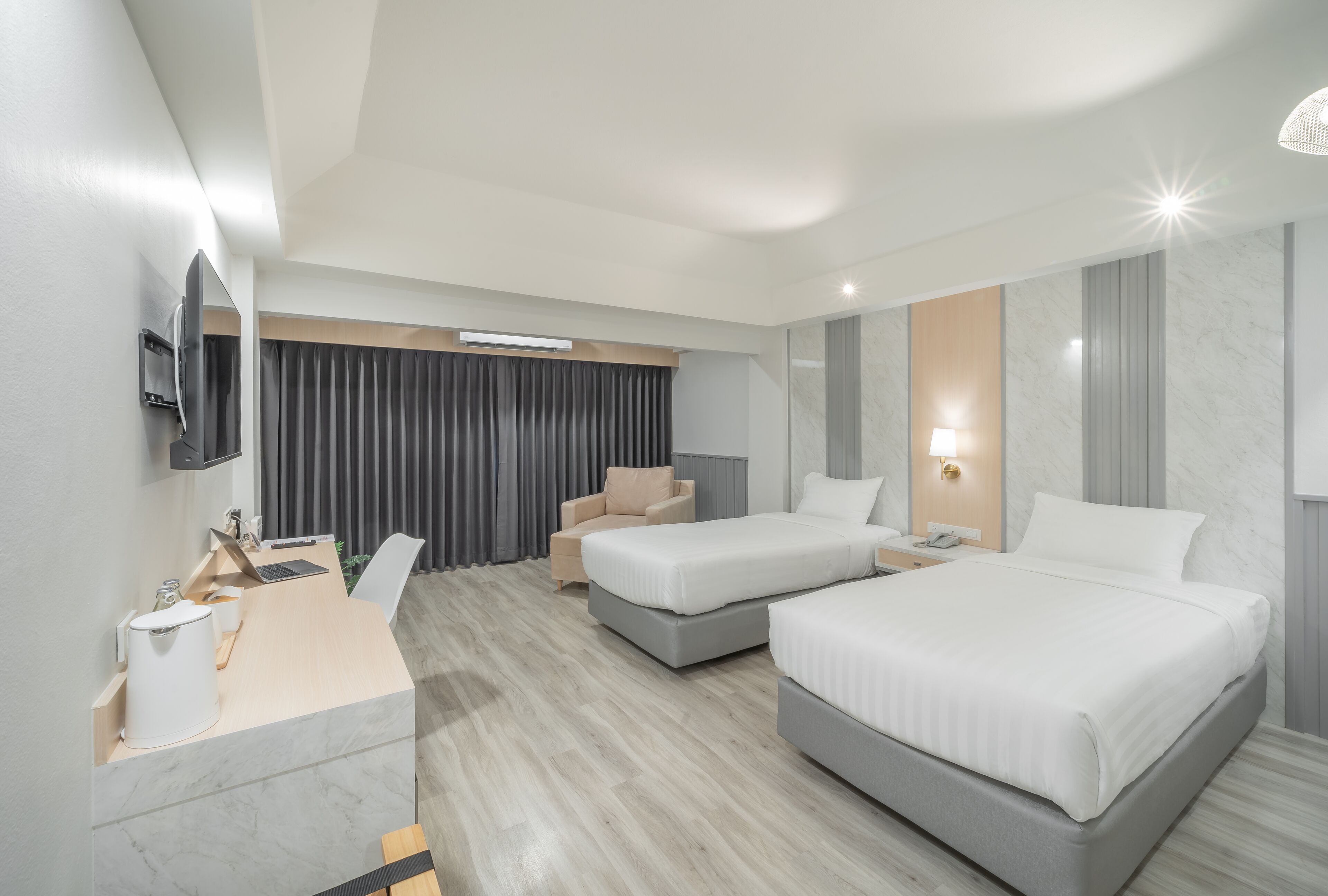 A modern hotel room with two beds, a desk with a laptop, a chair, and a TV mounted on the wall.