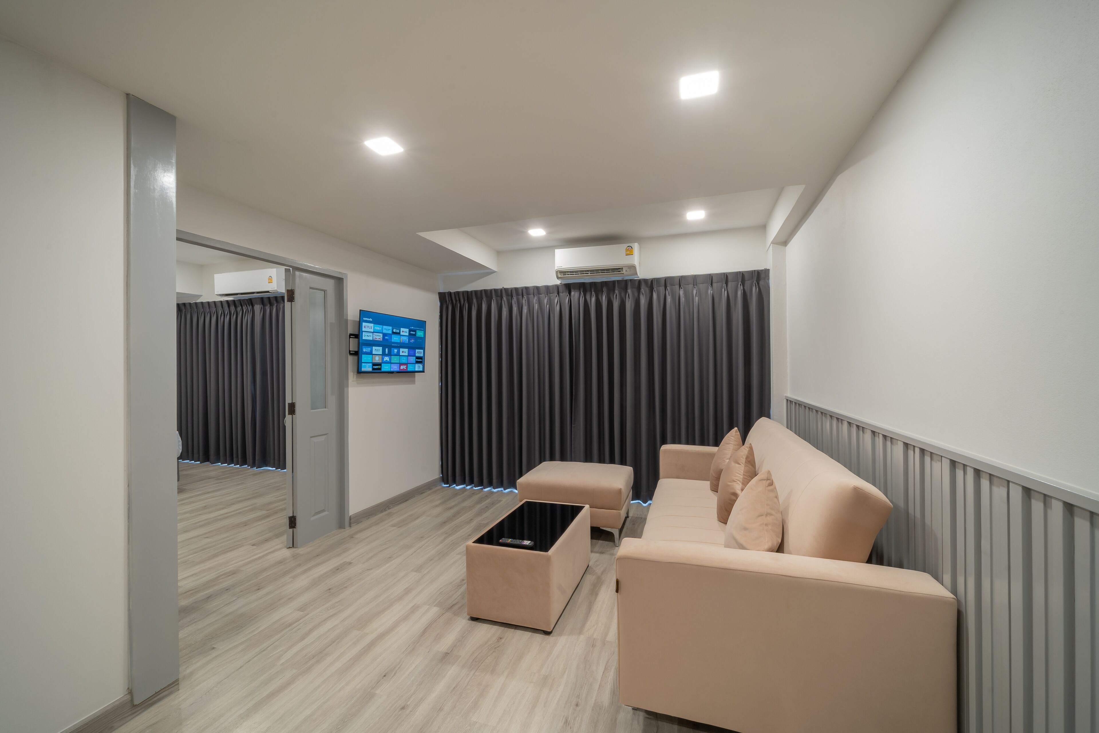 A modern living room with a beige sofa, a coffee table, and a flat-screen TV mounted on the wall.