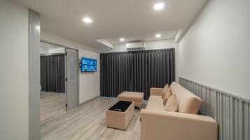 A modern living room with a beige sofa, a coffee table, and a flat-screen TV mounted on the wall.