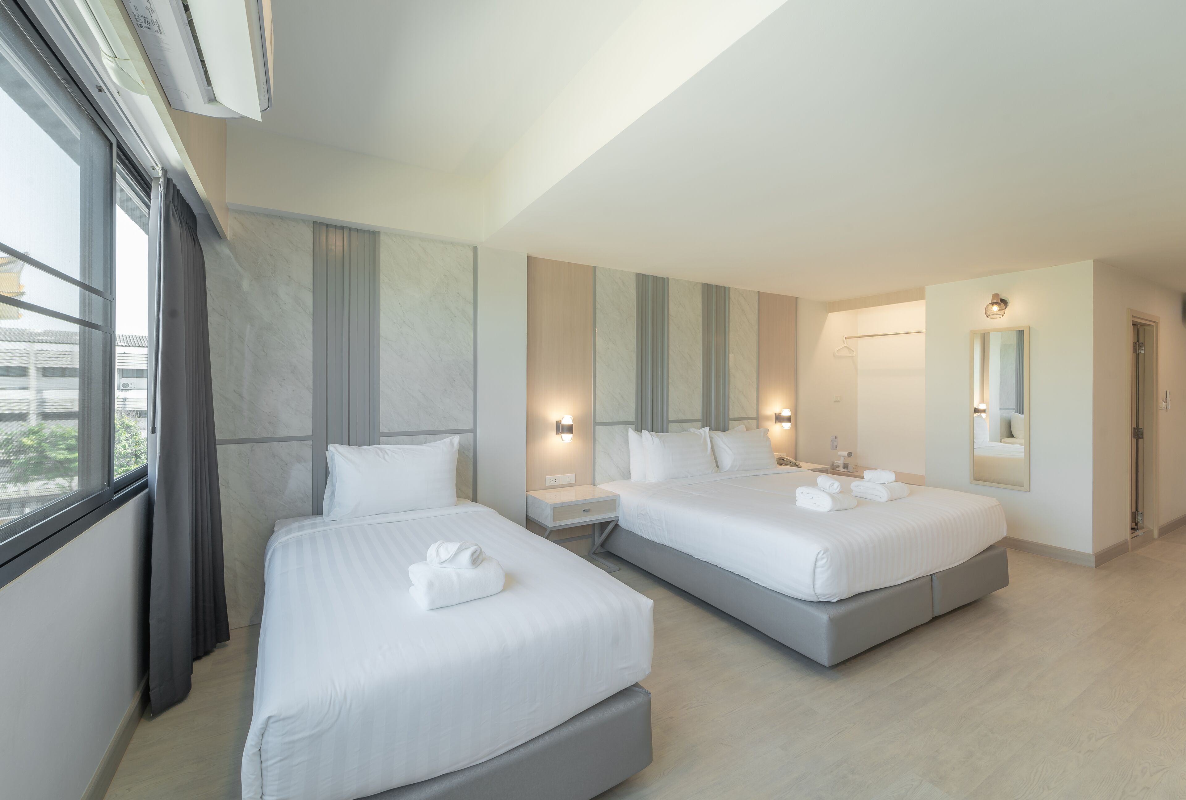 Quarto de hotel moderno com duas camas, uma janela grande e um espelho.