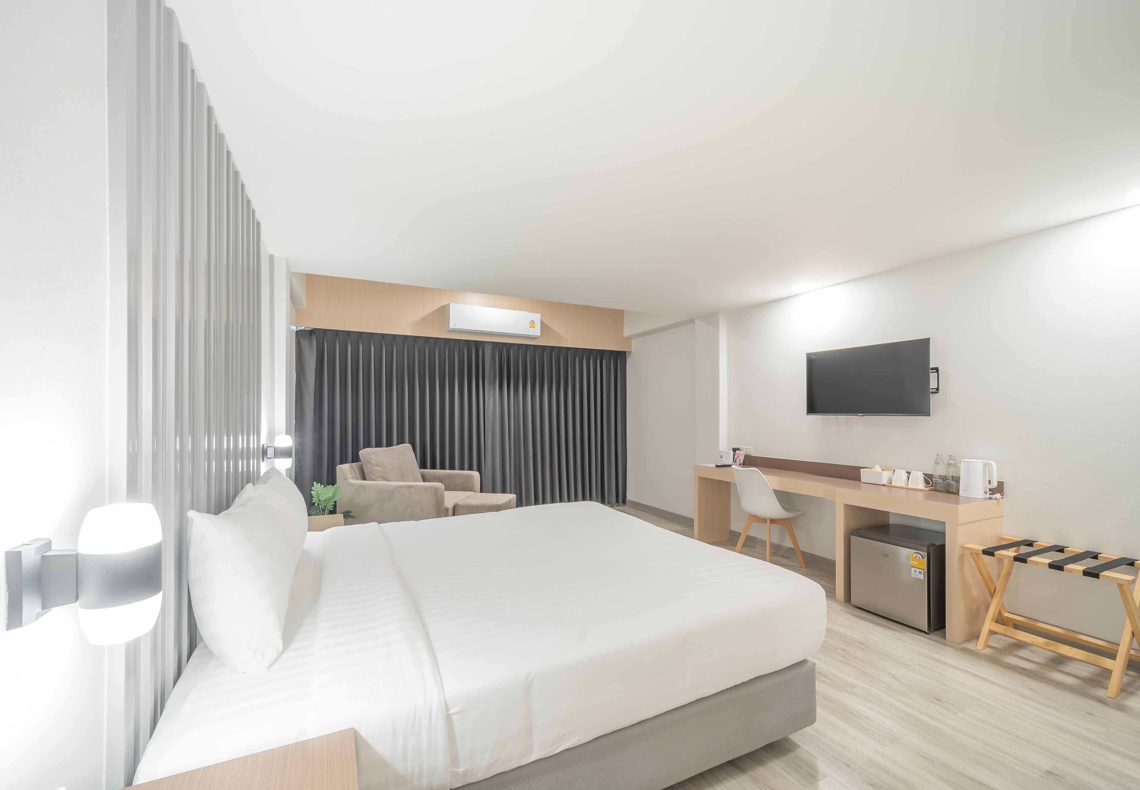 Una habitación de hotel moderna con una cama grande, un escritorio, una silla, un televisor y una pequeña kitchenette.