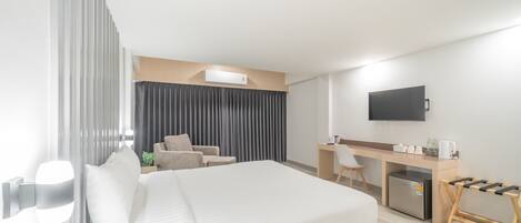 Una habitación de hotel moderna con una cama grande, un escritorio, una silla, un televisor y una pequeña kitchenette.