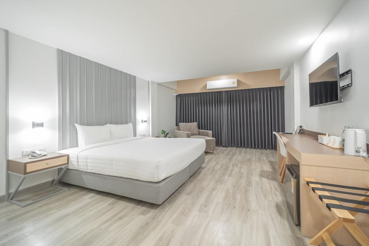 Une chambre d’hôtel moderne dotée d’un grand lit, de tables de chevet, d’un bureau, d’une chaise, d’un téléviseur à écran plat et d’une machine à café intégrée.