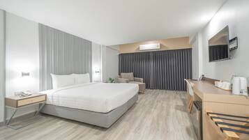 A modern hotel room with a large bed, bedside tables, a desk, a chair, a flat-screen TV, and a built-in coffee machine.
