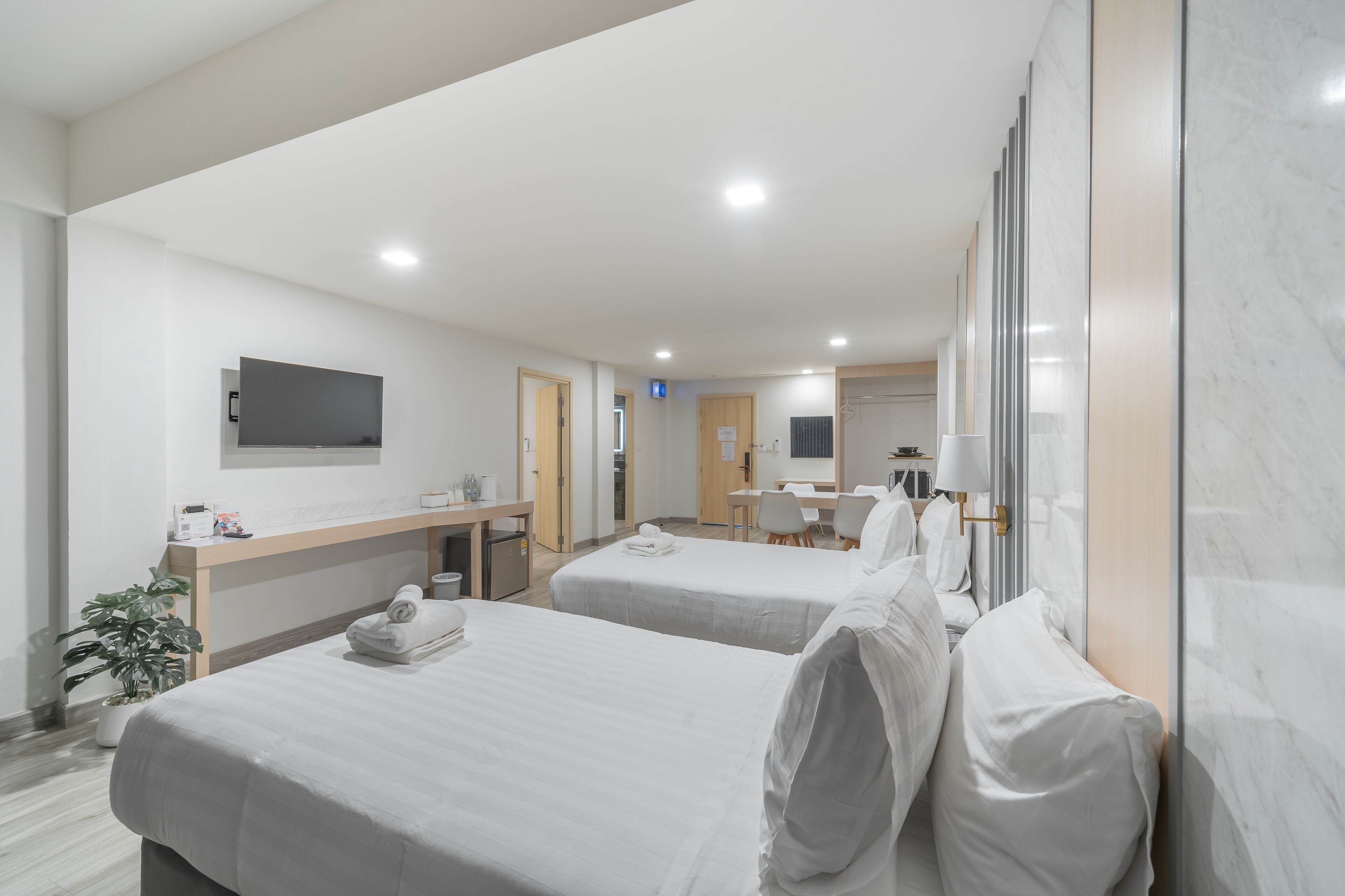 A hotel room with two beds, a desk, a TV, and a bathroom visible in the background.