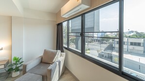 A modern room with a large window, a sofa, a potted plant, and an air conditioning unit. - The Space Hotel Lampang (Lampang)