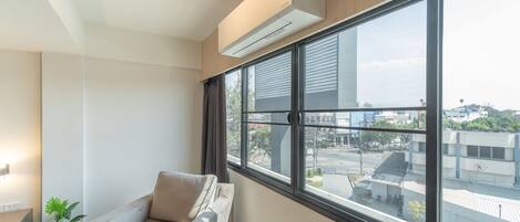 A modern room with a large window, a sofa, a potted plant, and an air conditioning unit.
