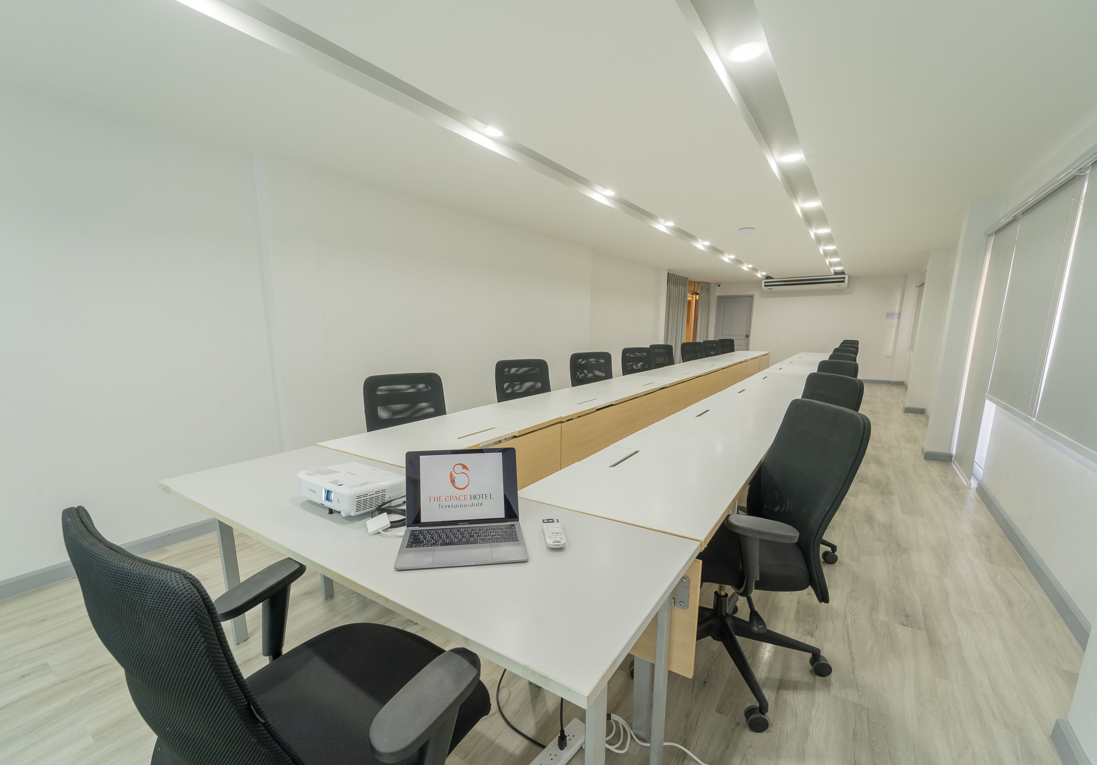 Una sala de conferencias con una larga mesa, sillas, una computadora portátil y un proyector.