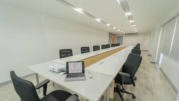 Una sala de conferencias con una larga mesa, sillas, una computadora portátil y un proyector.
