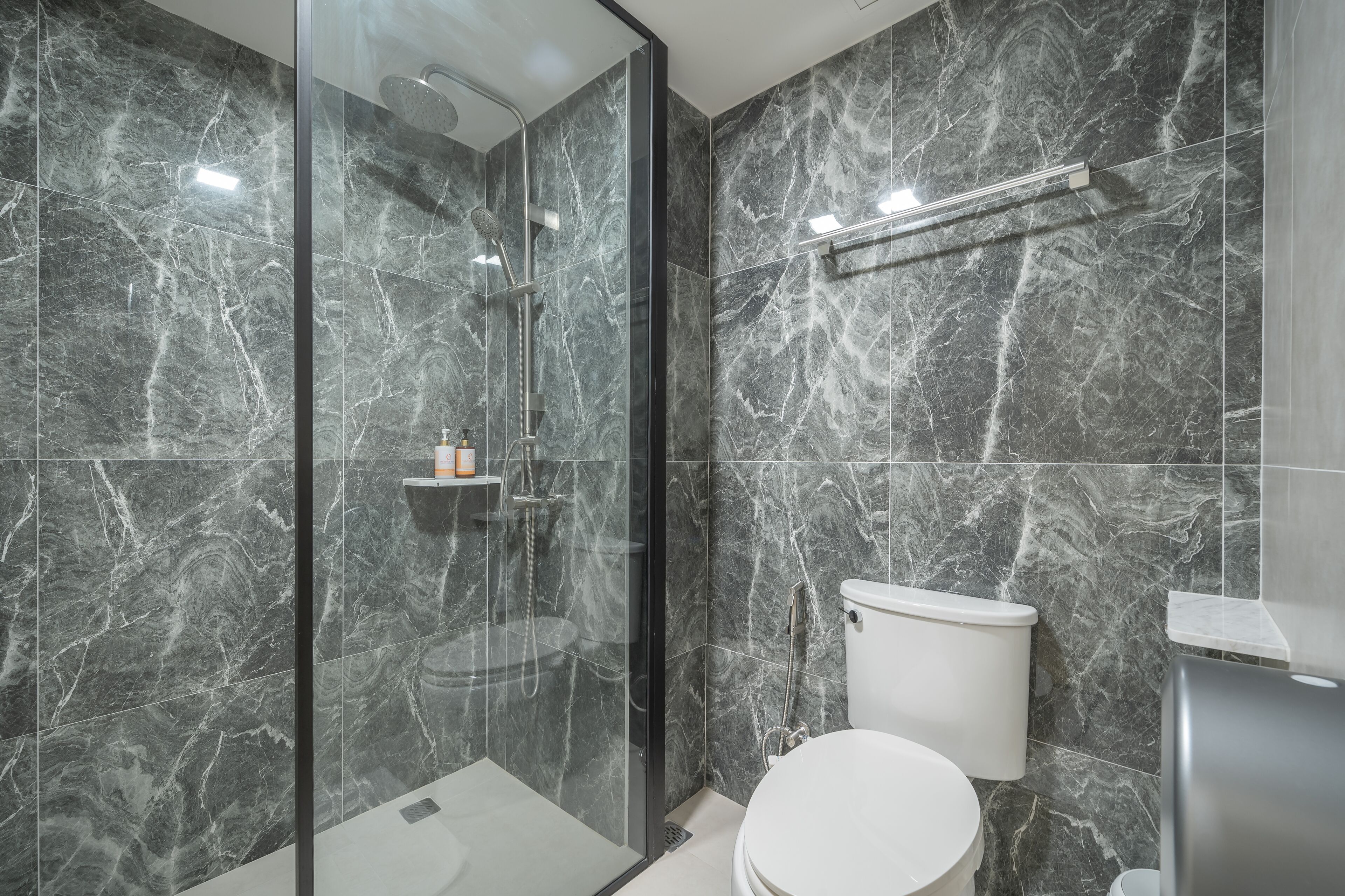 A modern bathroom with a glass-enclosed shower, a toilet, and a marble backsplash.